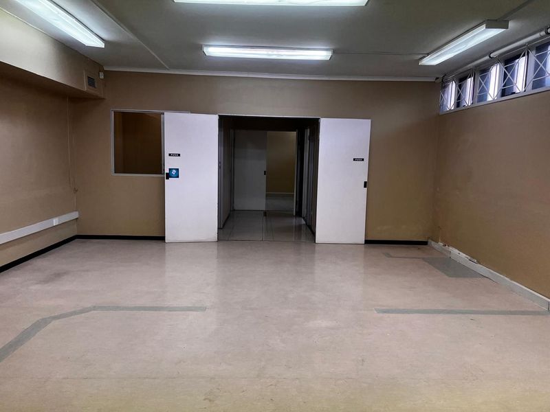 An empty, open-plan retail or office space featuring vinyl flooring, fluorescent lighting, and double-door access, ready for custom fit-out.