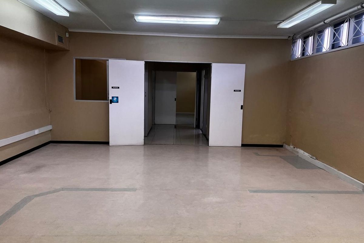 An empty, open-plan retail or office space featuring vinyl flooring, fluorescent lighting, and double-door access, ready for custom fit-out.