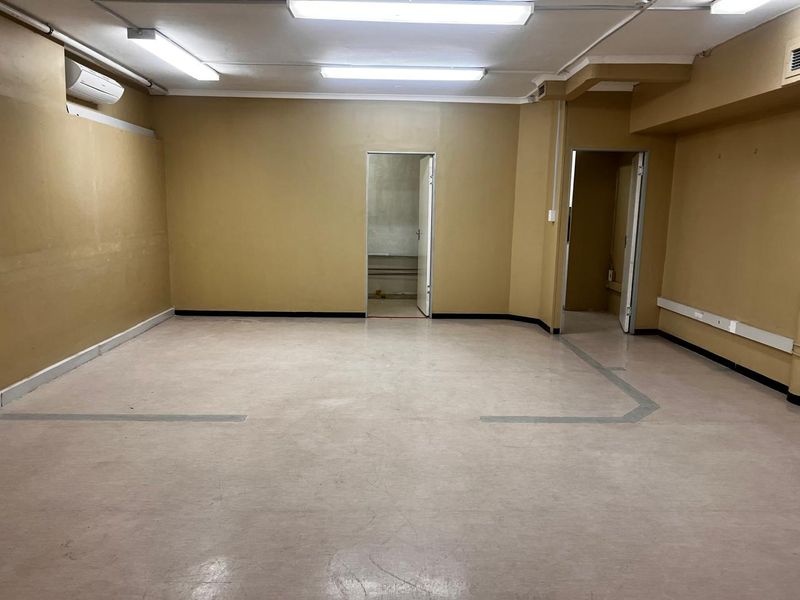 An empty, functional utility space featuring vinyl flooring, fluorescent lighting, and a wall-mounted air conditioning unit.