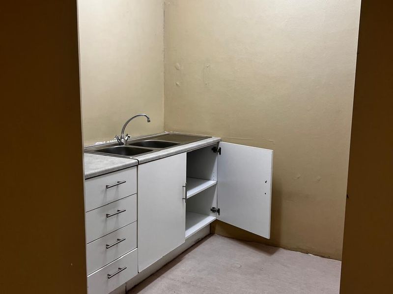 A compact scullery or utility area featuring built-in cabinetry, a stainless steel double sink, and neutral wall finishes.