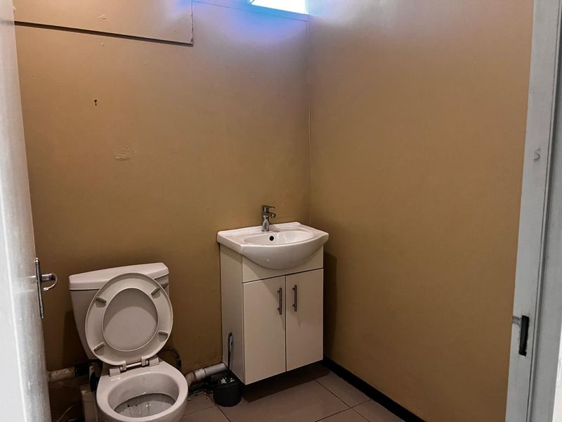 A small functional bathroom featuring a white vanity cabinet with a basin and a standard toilet, finished with tiled flooring and painted walls.