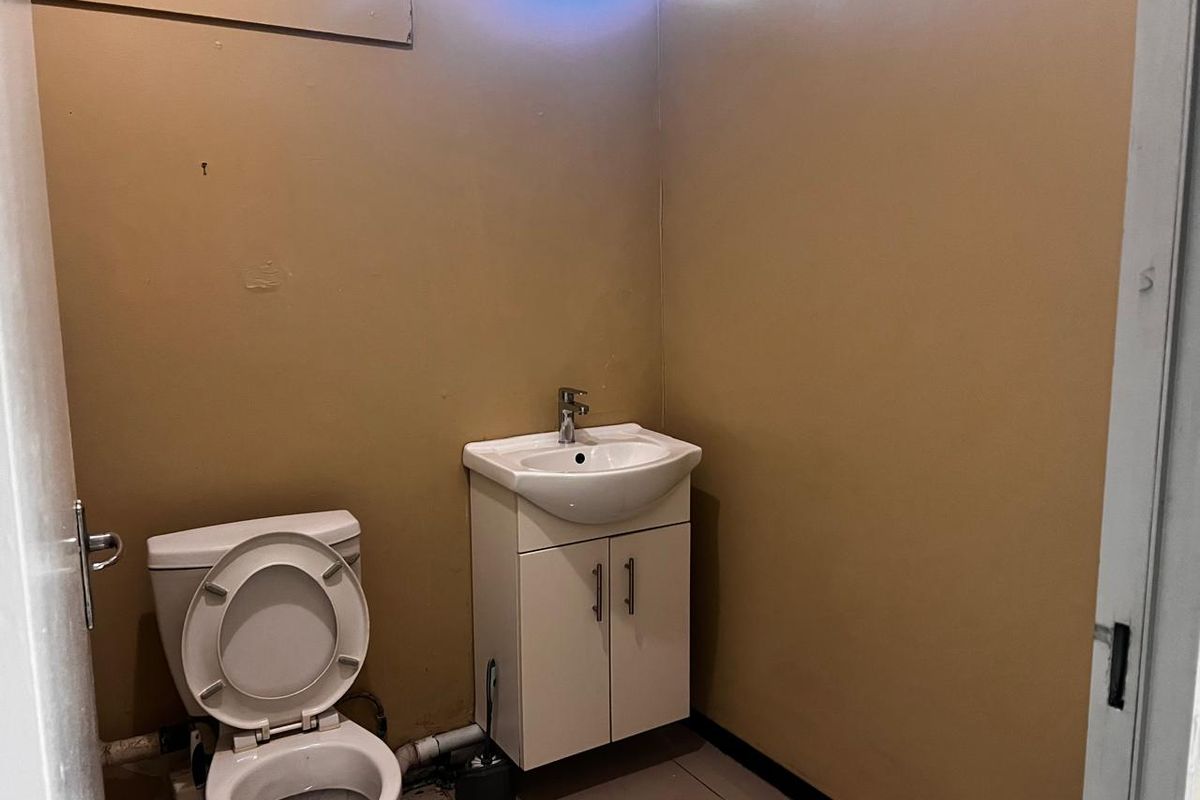A small functional bathroom featuring a white vanity cabinet with a basin and a standard toilet, finished with tiled flooring and painted walls.