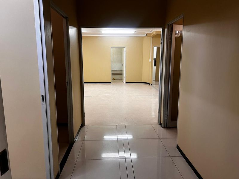 A vacant hallway with tiled flooring leading into an open-plan retail or office space with neutral wall finishes.