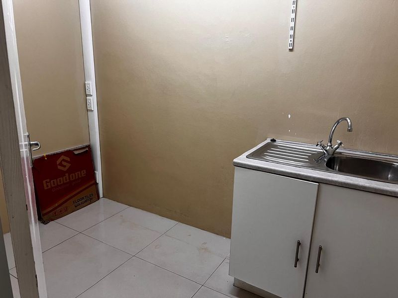 A functional scullery or utility area featuring a stainless steel sink, base cabinetry, and tiled flooring, suitable for additional prep or wash-up space.