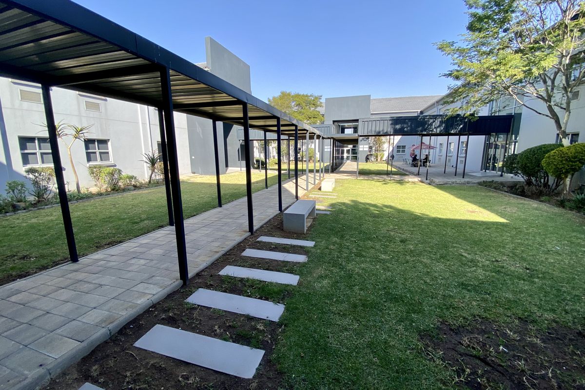 A well-maintained outdoor courtyard featuring a paved walkway with a covered metal pergola, manicured lawn, and integrated concrete seating.