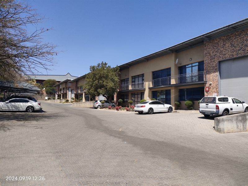 Exterior view of a multi-unit industrial complex featuring brick facades, roller shutter doors, and paved parking areas.