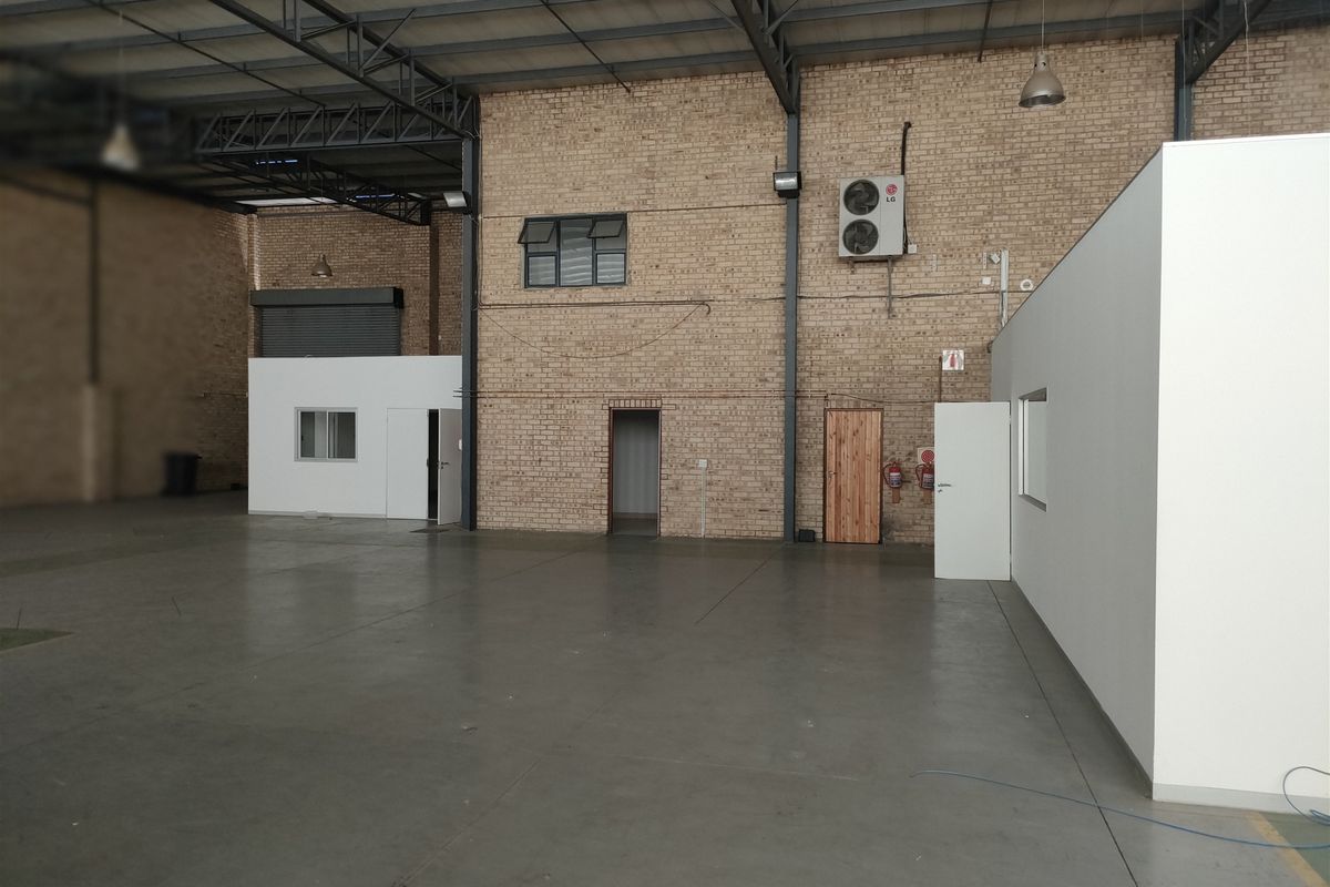 Spacious industrial warehouse unit featuring high ceilings with exposed steel trusses, durable concrete flooring, facebrick walls, and integrated office partitioning.
