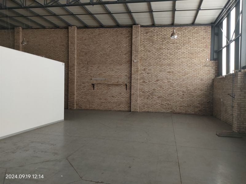 Spacious industrial utility area featuring exposed brick walls, high ceilings with steel trusses, concrete flooring, and ample natural light from large windows.