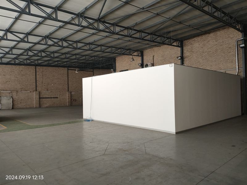 Spacious industrial warehouse unit featuring exposed steel roof trusses, brick walls, polished concrete flooring, and a central partitioned office structure.
