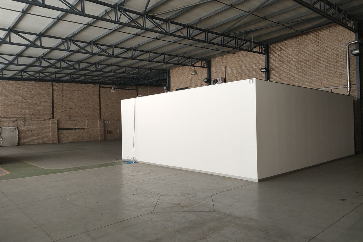 Spacious industrial warehouse unit featuring exposed steel roof trusses, brick walls, polished concrete flooring, and a central partitioned office structure.