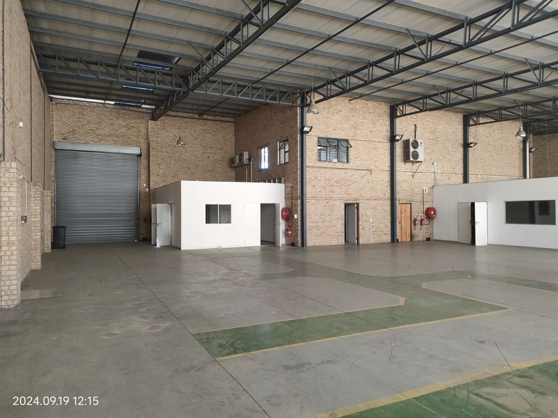 Spacious industrial warehouse featuring high exposed steel trusses, durable concrete flooring, facebrick walls, and a large roller shutter door for easy access.