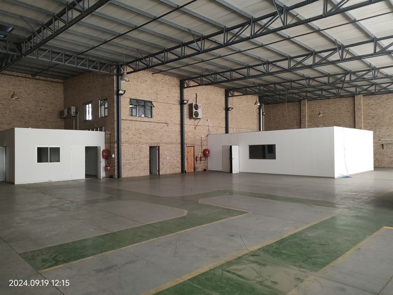 Spacious industrial warehouse featuring exposed steel roof trusses, concrete flooring, internal office partitions, and exposed brick walls, suitable for various commercial or storage operations.