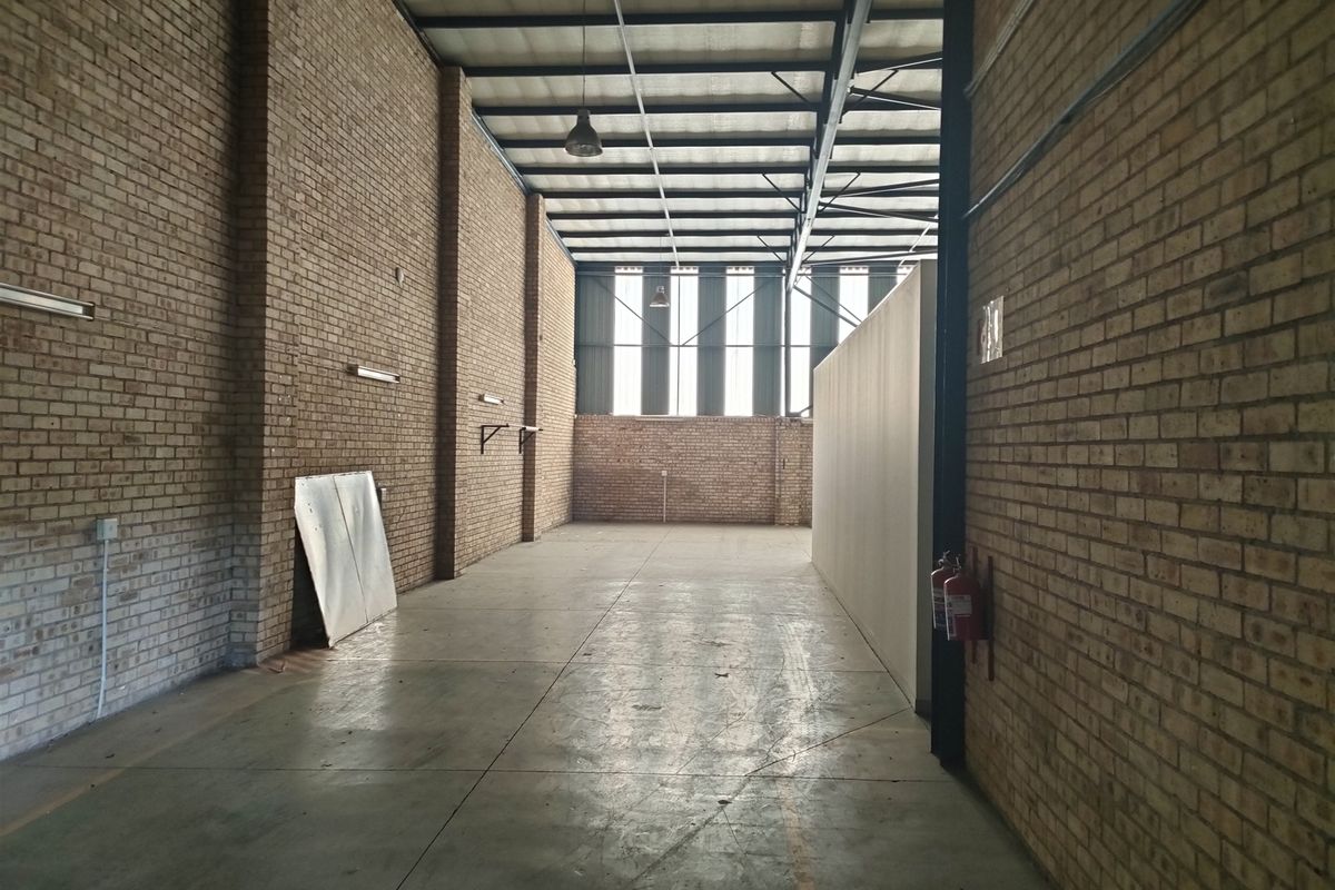 Spacious industrial utility area featuring exposed brick walls, concrete flooring, and high-clearance steel roof trusses, suitable for storage or workshop use.