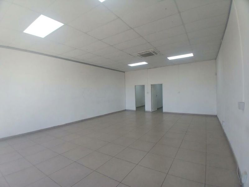 A spacious, empty office area featuring tiled flooring, a suspended ceiling with recessed lighting, and integrated air conditioning.