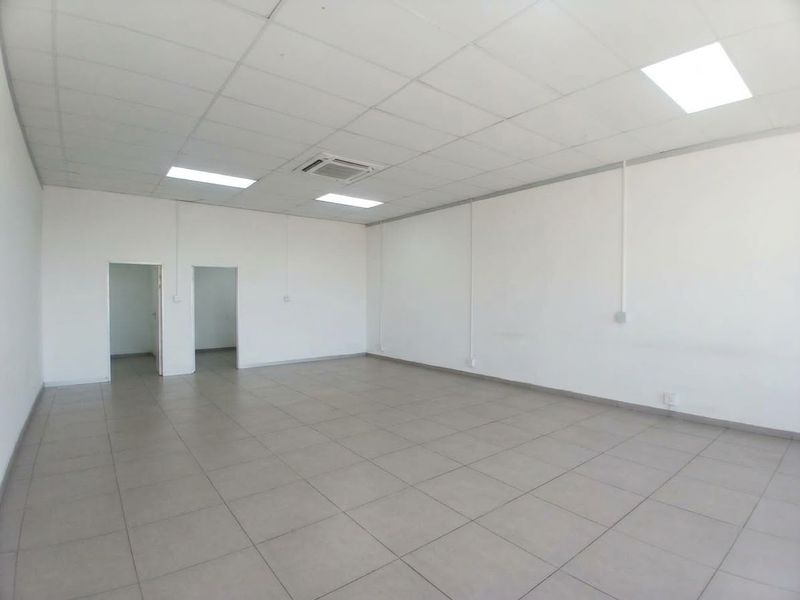 A spacious, empty office unit featuring neutral tiled flooring, a clean suspended ceiling with recessed lighting, and integrated ducted air conditioning.