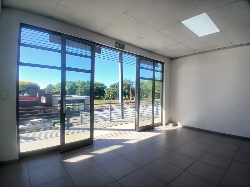 Bright and spacious empty office unit featuring tiled flooring, suspended ceiling, and large glass sliding doors leading to a balcony.