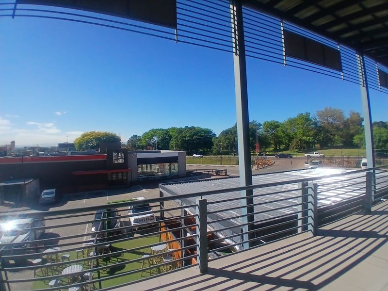 A spacious covered balcony with metal balustrades, offering an elevated view of the surrounding office park and parking area.