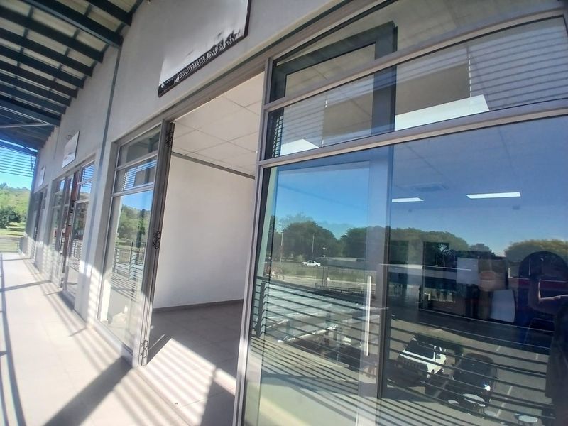Modern office entrance featuring large aluminum-framed glass doors, a covered tiled walkway, and an exposed steel roof structure.