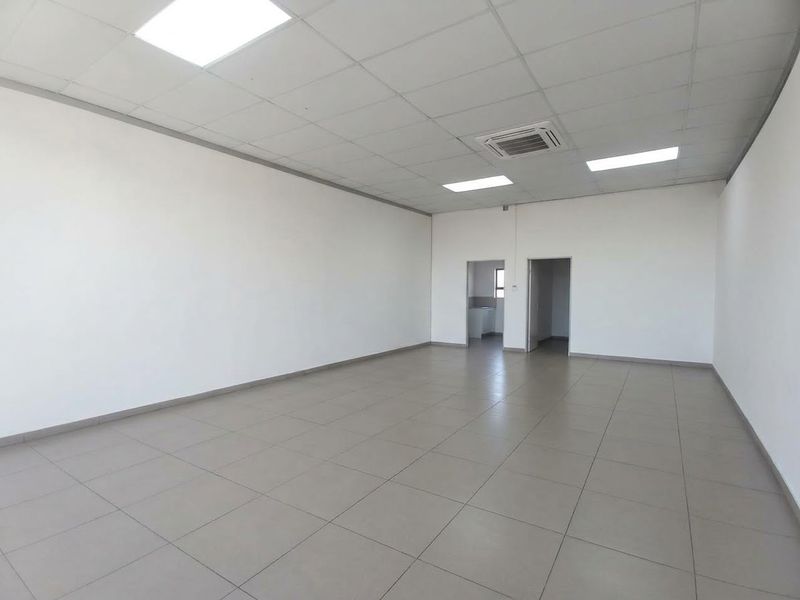A spacious, empty office area featuring neutral tiled flooring, a suspended ceiling with recessed lighting, and integrated ducted air conditioning.