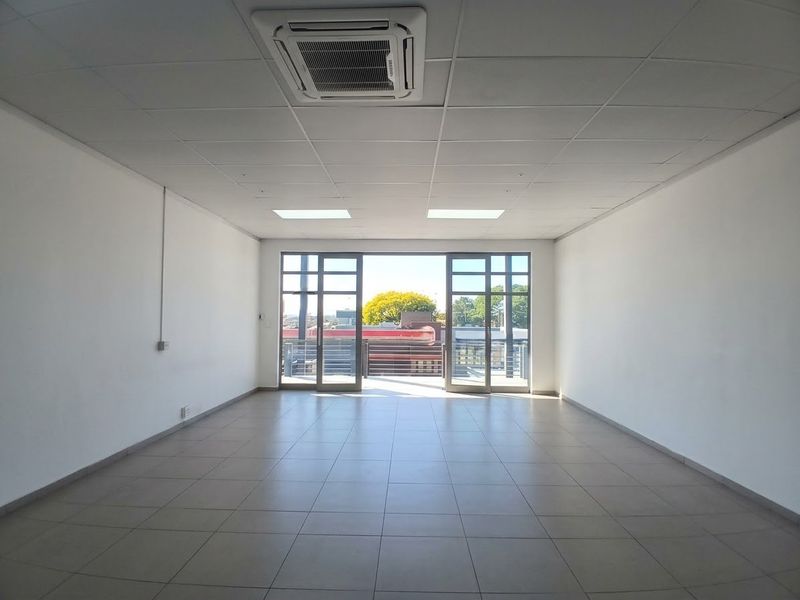 A bright, open-plan office space featuring tiled flooring, a suspended ceiling with integrated air conditioning, and large glass doors leading to an outdoor area.