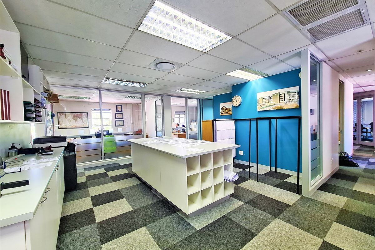 A professional office space featuring a central built-in workstation, glass partitioning, suspended ceiling tiles, and modern carpet tiling.