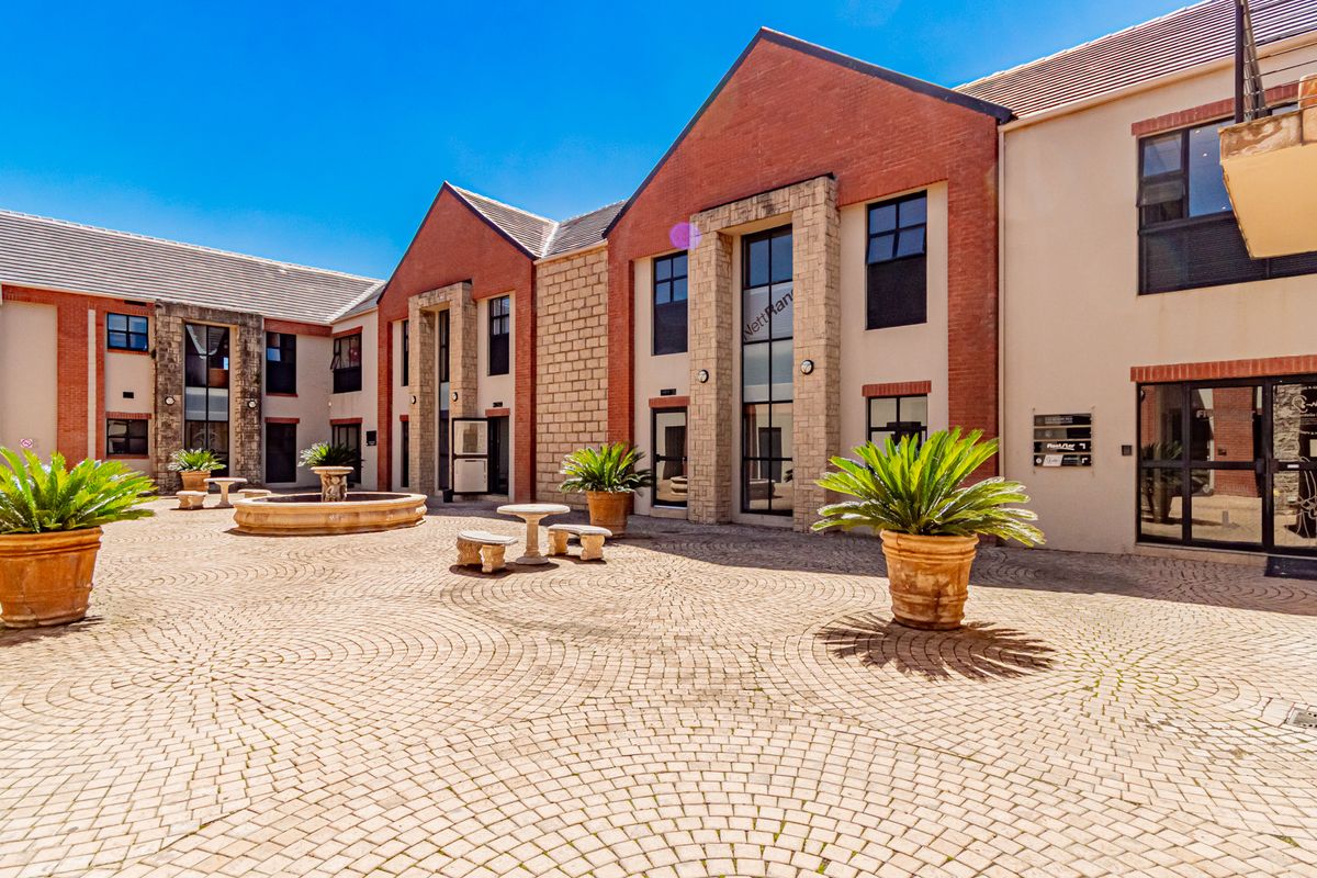A well-maintained office courtyard featuring decorative brick and stone architecture, a central stone fountain, and paved ground surfaces.
