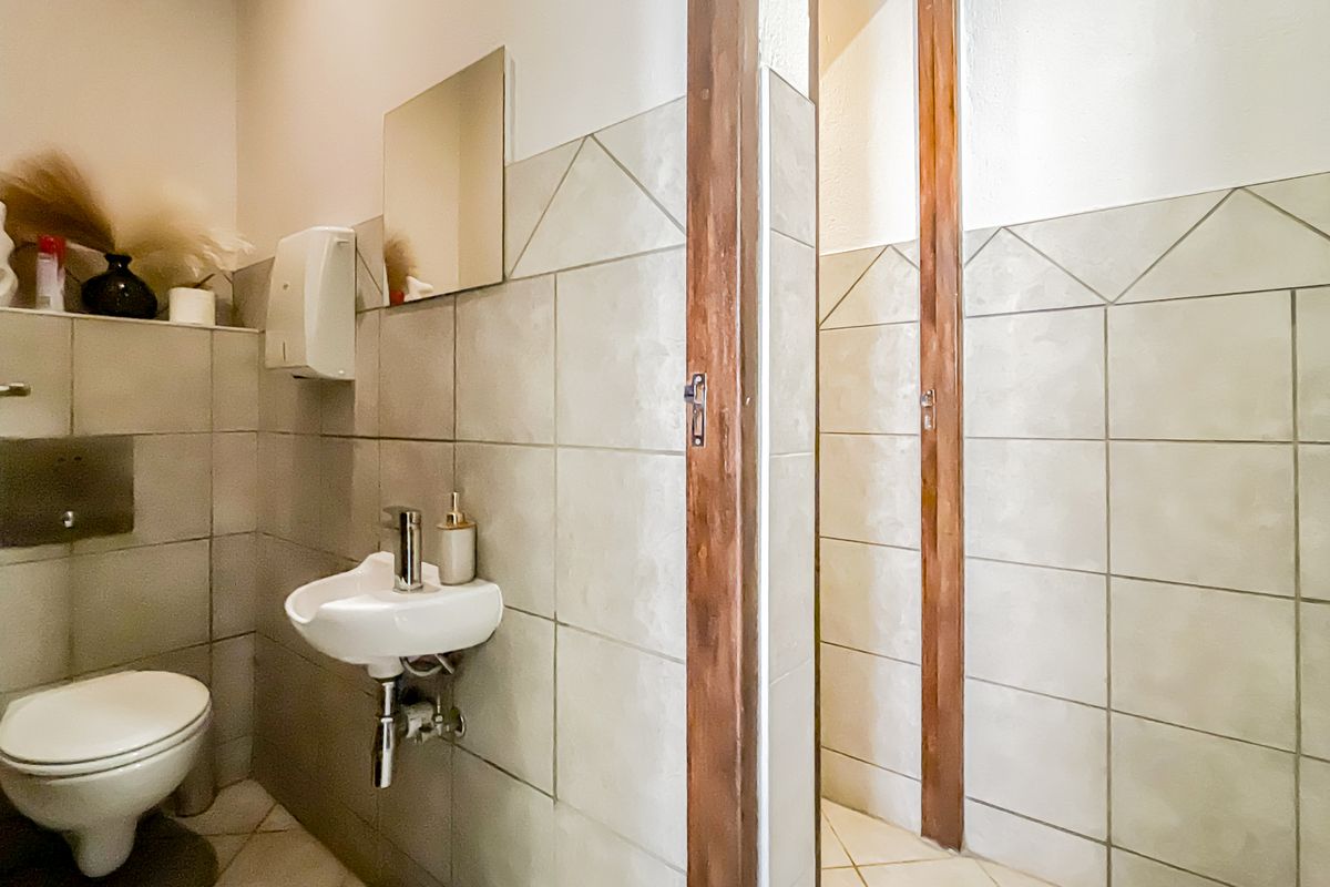 A functional office bathroom featuring tiled walls, a wall-mounted basin, and a toilet, with wooden door frames and neutral finishes.