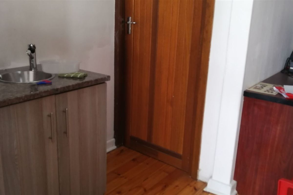 A compact kitchenette area featuring built-in cabinetry, a granite countertop with a stainless steel sink, and timber flooring.