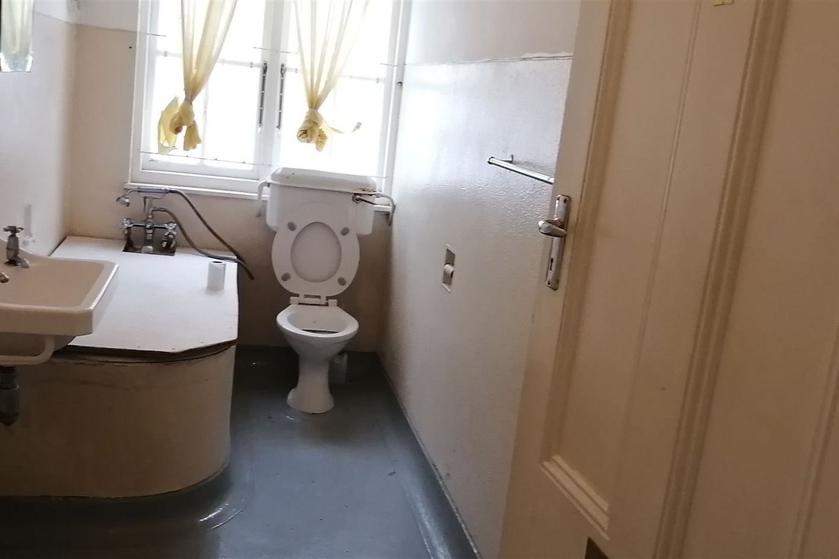 A dated bathroom featuring a wall-mounted basin, toilet, and built-in vanity unit, requiring modernization and cosmetic updates to improve its condition.