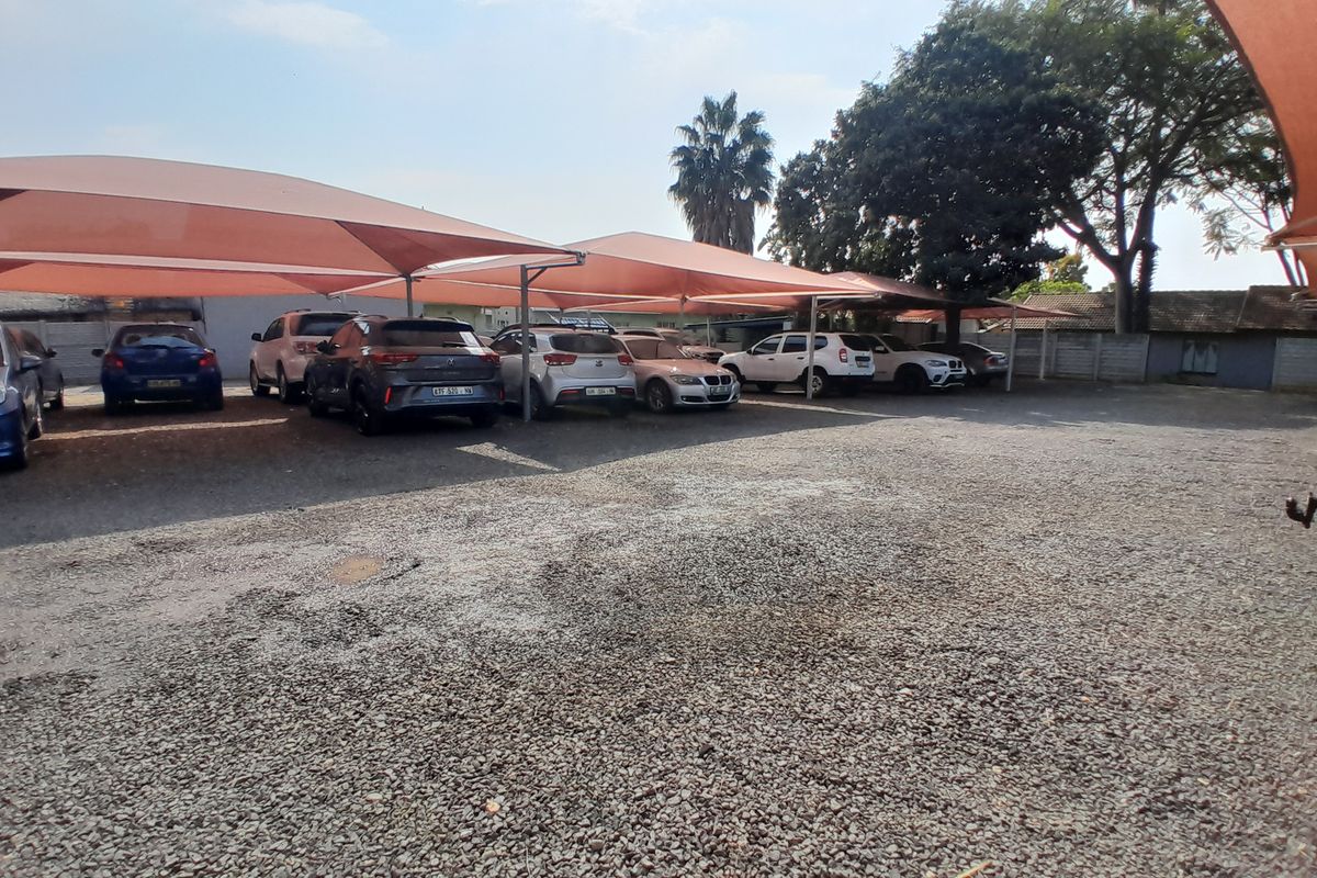 Outdoor parking area featuring multiple shade-cloth carports providing covered vehicle storage on a gravel surface.