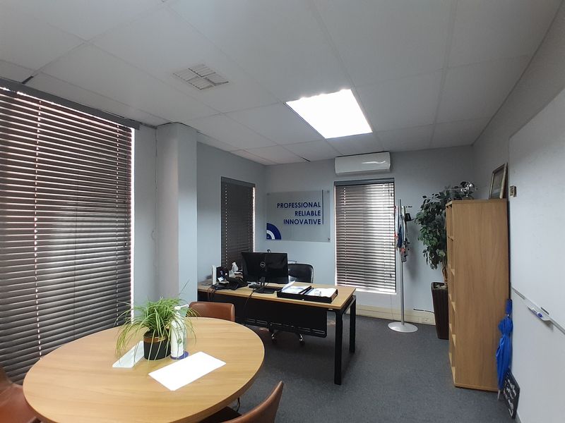 A functional office space featuring a drop ceiling, recessed lighting, wall-mounted air conditioning unit, and window blinds.