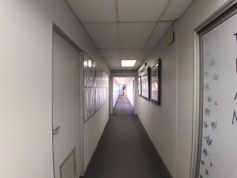 A long commercial office hallway featuring neutral walls, carpeted flooring, and a drop ceiling with integrated lighting.