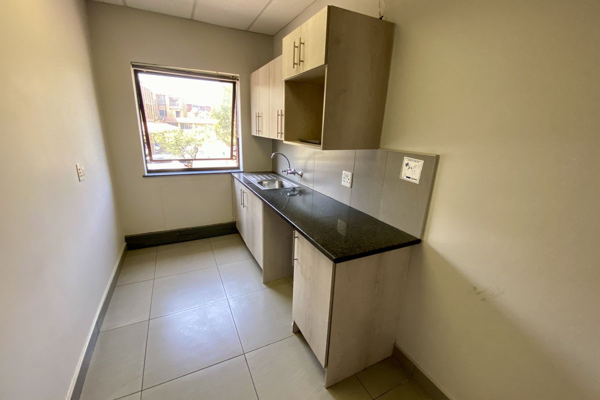 A compact kitchenette featuring light wood-finish cabinetry, a dark granite countertop, a stainless steel sink, and tiled flooring.