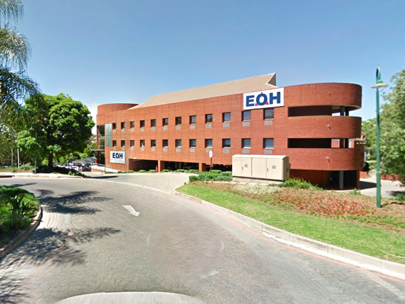 Exterior view of a multi-story industrial brick office building with prominent corporate branding and paved driveway access.