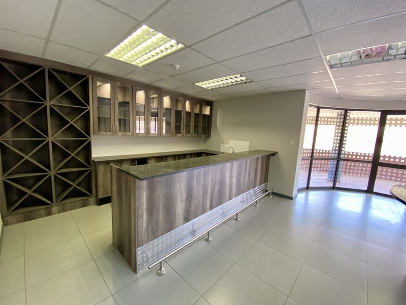 A well-maintained bar area featuring built-in cabinetry, a stone-topped counter, integrated wine storage, and tiled flooring, suitable for office or industrial hospitality use.