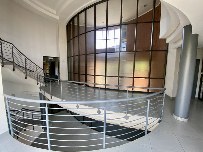 Spacious industrial building foyer featuring a curved glass curtain wall, tiled flooring, and a modern metal staircase with integrated railings.