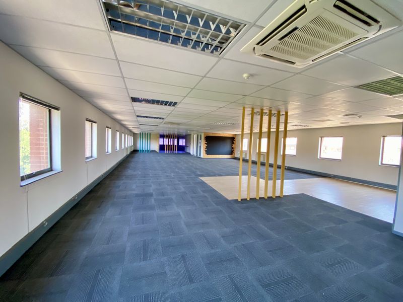 Spacious open-plan industrial office area featuring suspended ceilings, recessed lighting, integrated air conditioning units, and durable carpet tile flooring.