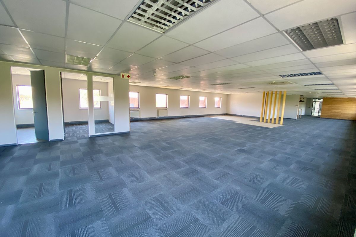 Spacious open-plan industrial office area featuring suspended ceiling tiles, recessed lighting, and carpeted flooring with partitioned office sections.
