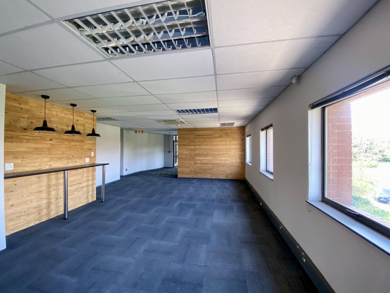 Spacious open-plan office area featuring wood-paneled accent walls, recessed ceiling lighting, carpeted flooring, and large windows providing natural light.