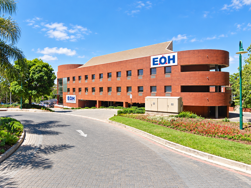 A professional exterior view of a multi-story industrial brick office building with a paved driveway and landscaped surroundings.