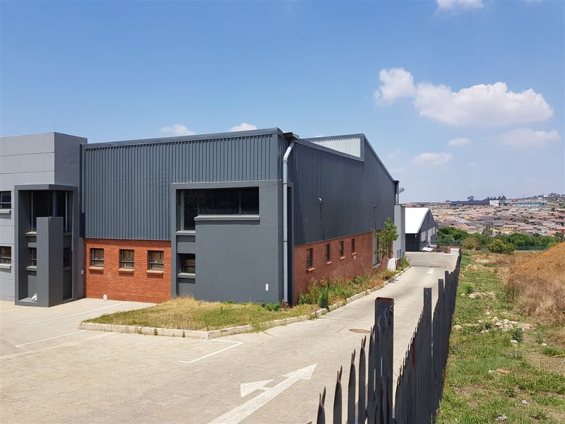 Exterior view of an industrial property featuring a combination of corrugated metal cladding and face brick masonry with an adjacent paved driveway.