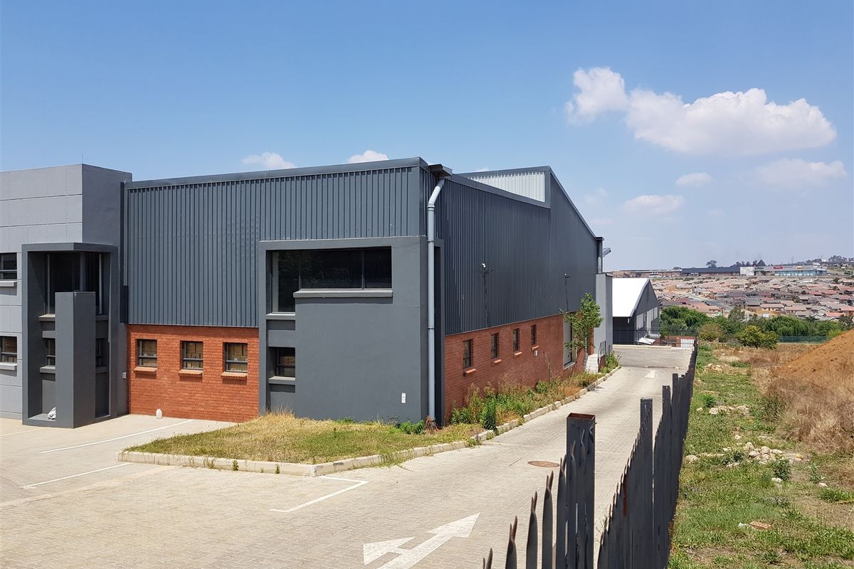 Exterior view of an industrial property featuring a combination of corrugated metal cladding and face brick masonry with an adjacent paved driveway.