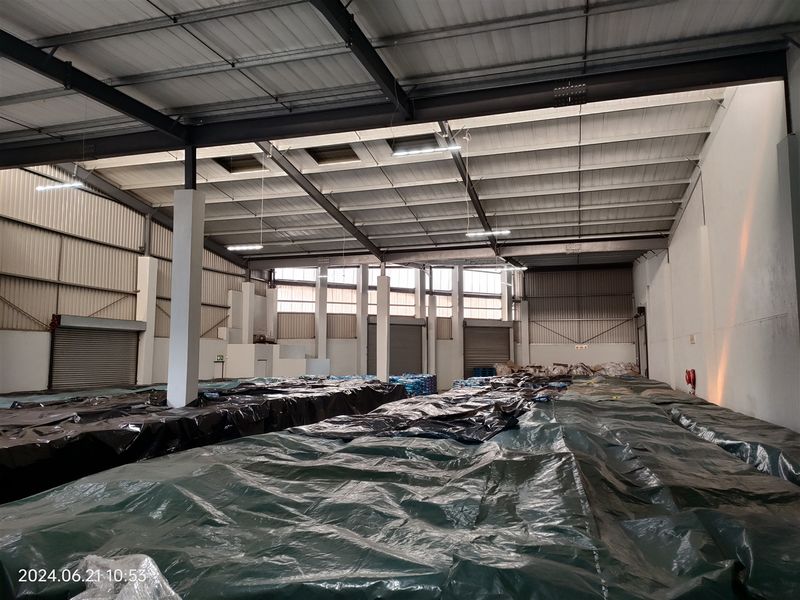 Spacious industrial warehouse featuring a high-clearance steel portal frame, corrugated metal roofing, multiple roller shutter doors, and functional high-bay lighting.