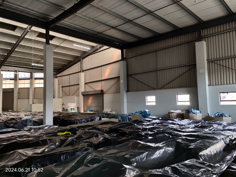 Spacious industrial warehouse featuring a high-clearance steel portal frame, corrugated metal roofing, concrete support columns, and a functional roller shutter door.