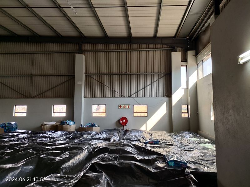 Spacious industrial warehouse unit featuring high ceilings, exposed steel structural elements, corrugated metal wall cladding, and natural light through high-level windows.