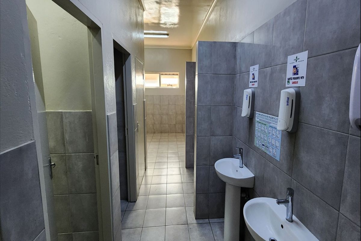 A functional industrial restroom facility featuring tiled walls, pedestal basins, and multiple partitioned cubicle entrances.