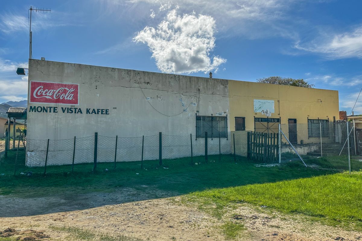 Exterior view of a retail building featuring a large painted sign, security bars on windows, and a surrounding wire mesh fence.