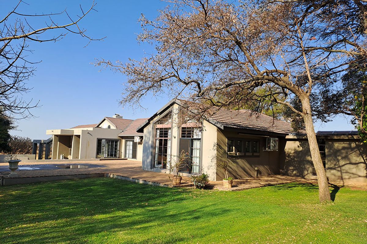 Rear view of the farm property featuring a spacious paved patio, swimming pool, and large windows overlooking the landscaped garden.