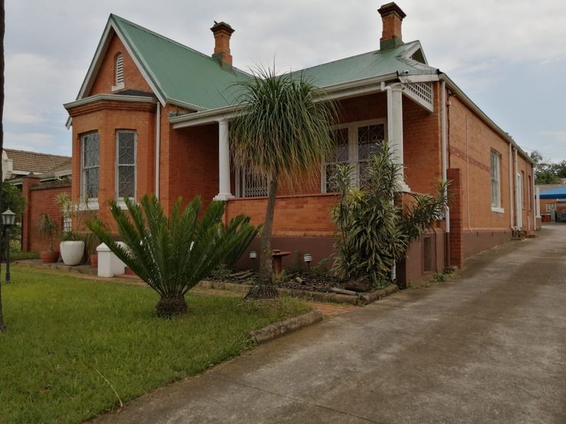 A classic brick commercial property featuring a green metal roof, covered veranda, and a concrete driveway approach.