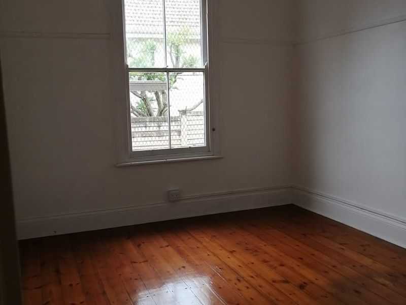 A bright, empty bedroom featuring polished timber flooring, classic picture rails, and a traditional sash window.